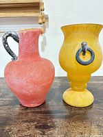 Front view of red frosted glass pitcher and yellow pedestal vase
