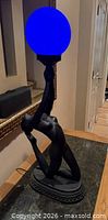 Full view of lamp lit, blue globe, cast metal figure on base