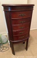 Closed armoire showing curved front, four drawers, fluted legs, dark cherry finish