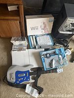 Overall view of Wii Balance Board, Guitar Hero controller, console packaging, stack of game cases, blue tray with accessories
