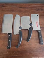 Group shot of all four stainless steel meat cleavers on wood surface