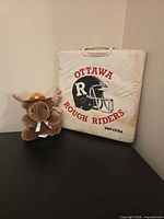 Front of stadium cushion with Ottawa Rough Riders helmet logo and plush moose