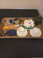 Tray showing all items: stamps tin, teacups and saucers, owl warmer, Finlandia glass, wooden spoon, bowl, coin purse, bracelets