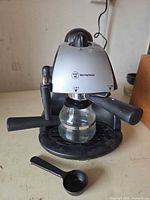 Front view of Westinghouse espresso machine with portafilter and glass carafe attached, coffee scoop in foreground