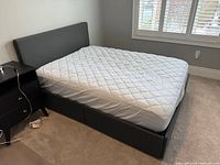 Full view of grey fabric double bed with mattress, headboard visible