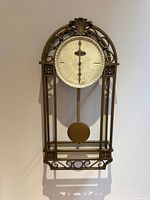 Full view of arched metal wall clock showing frame, dial and pendulum