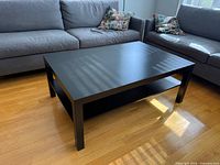 Overall view of black-brown rectangular coffee table between two grey sofas