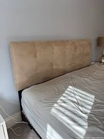 Front view of beige microsuede king headboard attached to bed frame
