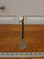 Full view of clear glass bottle with gold-tone giraffe head stopper next to ruler