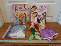 All three books and two plush dolls displayed on ruler for scale