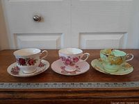 Three teacup and saucer sets side by side on ruler for scale