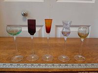 Front view of five cordial glasses lined next to ruler
