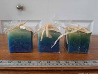Three wrapped square gradient candles beside ruler for scale