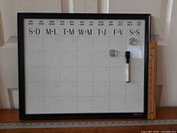 Front view of calendar board showing bilingual month headings, grid, magnets, marker and ruler for scale