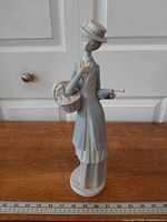 Full front view of porcelain figurine standing on wood surface with ruler for scale