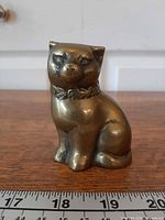 front view of brass cat figurine beside ruler