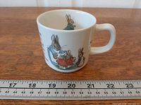 Mug side with Peter Rabbit illustration beside ruler for scale
