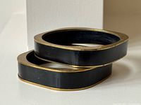 two stacked black bangles with brass edging, showing squared shape