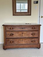 Full frontal view of chest showing marble top, three drawers, wood pulls, casters