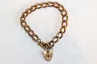 Full view of gold chain bracelet arranged in oval showing heart padlock clasp and safety chain