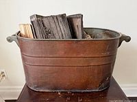 Front view of copper boiler tub with patina and firewood inside (firewood not included)