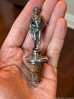 Front view of sterling silver figural bottle stopper showing missing hand and split cork