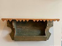 Front view of green painted wall shelf showing sawtooth edge and interior compartment