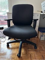 Front view of black adjustable office chair showing seat, backrest, armrests and caster base