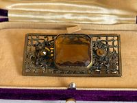 Front view of brooch in box showing amber glass stones and filigree brass frame