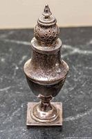 Full view of tarnished sterling silver pepper shaker showing urn form and square base