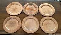Six hammered copper charger plates laid flat showing overall condition