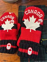 Two pairs Canada Olympic mittens on plaid scarf