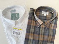 Front view of both shirts: packaged white L.L. Bean and folded brown plaid Harry Rosen