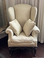 Front view of armchair with pillows, showing linen upholstery and carved wood base