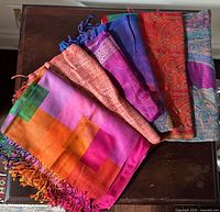 Stacked view of several patterned shawls showing block pattern, paisley, colors and fringes