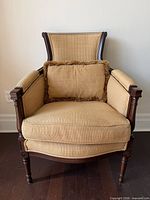 Front view of carved wood armchair with striped upholstery and fringed cushion