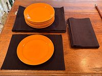 Stack of orange plates on black placemats with folded runner