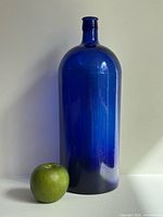 Front view of tall cobalt blue glass bottle beside green apple for scale