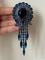 Front view of blue rhinestone waterfall brooch held in hand