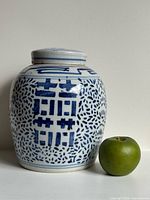 Front view of blue and white ginger jar beside apple for scale