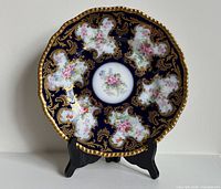 Front view showing cobalt ground, gilt scrolls, floral reserves, scalloped rim