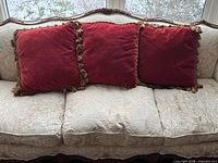 Three red velvet tassel-trim pillows displayed on sofa
