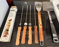 Six BBQ utensils and Weber box on countertop