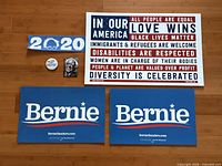 All six items: two blue Bernie yard signs, one "In Our America" sign, bumper sticker, button, sealed trading card pack