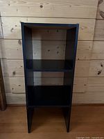 Front view of black vertical shelving unit showing open back and two shelves