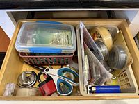 Overview of drawer showing all listed items including scissors, padlock, lighter, tapes, wire, can opener, and containers