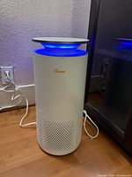 Full view of Crane white cylindrical air purifier plugged in, blue light on top