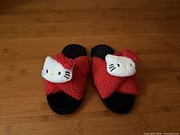 Top view of both slippers showing red fuzzy uppers, Hello Kitty plush heads, and black soles
