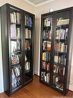 Two tall matching dark bookcases with glass doors filled with books