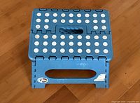 Top and side view of blue folding step stool showing anti-slip dots, handle, and sticker